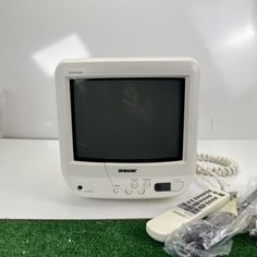 an old computer monitor sitting on top of a green carpet next to a remote control