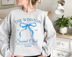 a woman sitting on top of a bed wearing a sweatshirt with the words, the winston social club