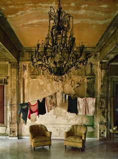 a chandelier hangs from the ceiling in an old room with two chairs and a couch