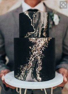 a black and gold wedding cake on a white plate with a man in a suit behind it