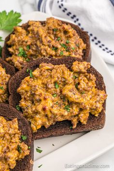 three pieces of bread with cheese and meat on them sitting on a plate next to parsley