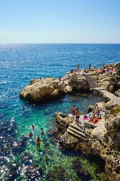 people are swimming in the ocean near some rocks and steps that lead into the water