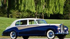 an old blue and white car is parked on the side of the road in front of some trees