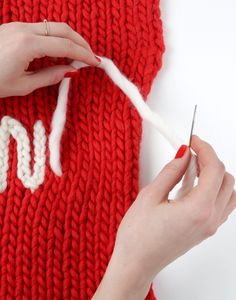 a woman is knitting the letters on a red knitted sweater with white stitchs