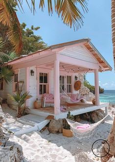 a small pink house on the beach with hammock and palm trees in front