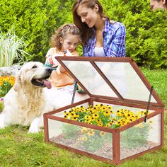 a woman sitting next to a child and a dog in a garden with sunflowers