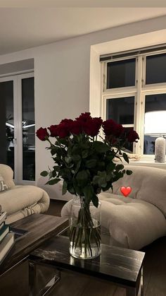 a vase filled with red roses sitting on top of a table next to a couch