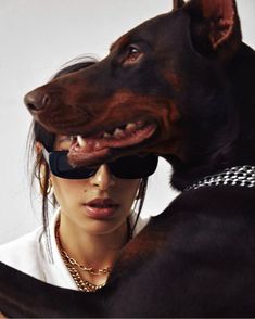 a woman wearing sunglasses and holding a large black dog in her arms, both looking at the camera