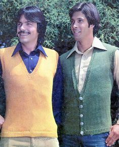 two men standing next to each other in sweaters and vests with trees in the background