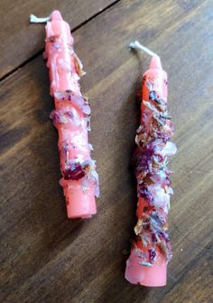 two pink candles sitting on top of a wooden table next to each other, covered in food