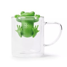 a glass mug with a green frog in it's mouth