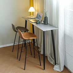 a desk with a laptop on it next to two stools in front of a window