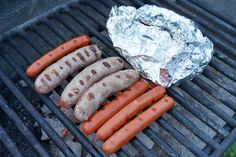 hot dogs and sausages are cooking on a grill with tin foil wrapped around them