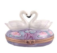 two white swans sitting on top of a pink and purple box with gold trimming