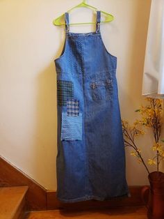 a denim dress hanging on a wall next to a potted plant with yellow flowers