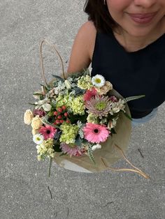 a woman holding a bouquet of flowers in her hand on the ground with concrete behind her