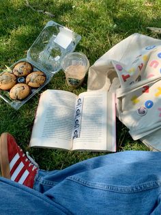 an open book sitting on top of a grass covered field next to muffins