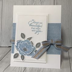 a handmade card with blue flowers and ribbon on it, sitting on a wooden surface