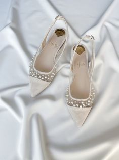 a pair of white high heeled shoes with pearls on the toes and heels are laying on a white satin surface