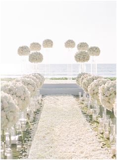 the aisle is lined with white flowers and candles for an outdoor ceremony at the beach