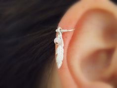 a close up of a person's ear with a small silver feather on it