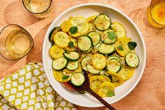 a white bowl filled with sliced cucumbers next to two glasses and napkins