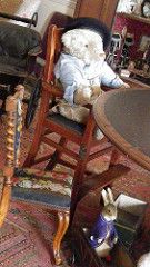 a teddy bear sitting in a rocking chair next to a table with other stuffed animals on it