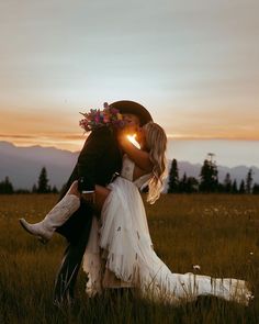 a bride and groom kissing in the middle of a field at sunset with mountains in the background