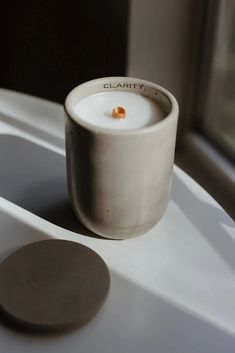 a white cup sitting on top of a sink next to a window with a candle in it