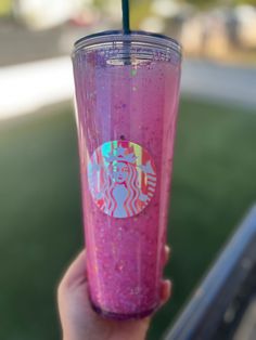 a hand holding a pink starbucks drink with glitter on the lid and straw in it