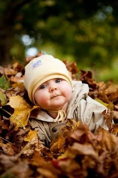 a baby laying on top of leaves in the grass and wearing a beanie hat