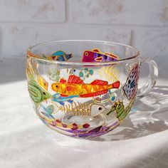 a glass cup with colorful fish painted on the inside and bottom, sitting on a white surface