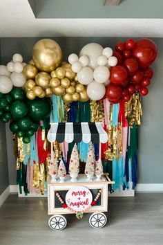 a cart with balloons and streamers on it in front of a wall that says happy birthday