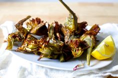 a white plate topped with cooked artichokes next to a lemon wedge