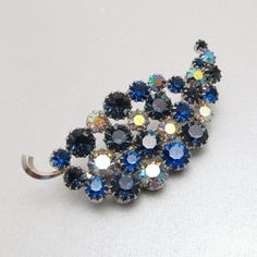 Vintage blue rhinestone leaf has varying colors of blue stones in all prong settings and set in silver tone metal.  Nice sparkle from some ab coated stones.  Measures about 2 1/2 inches X 1 1/4 inch. Unsigned, excellent vintage condition.  (Matching earrings listed separately)Find lots more vintage jewelry at Purple Daisy Jewelry!http://www.etsy.com/shop/purpledaisyjewelryThanks a bunch for shopping for vintage jewelry at Purple Daisy Jewelry on Etsy! Blue Crystal Brooches With Rhinestones, Costume Jewelry Blue Brooches With Rhinestones, Daisy Jewelry, Vintage Rhinestone Brooch, Purple Daisy, Leaf Brooch, Blue Stones, Bird Jewelry, Brooch Jewelry