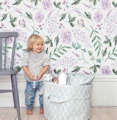 a little boy standing in front of a flowered wallpaper with a basket full of toys