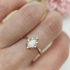 a woman's hand wearing a gold ring with a white stone and diamond accent