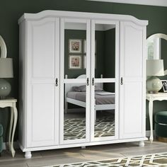 a white armoire with mirrored doors in a green room next to a chair and table