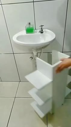 a bathroom with a sink, toilet and hand held over the wall by a towel dispenser