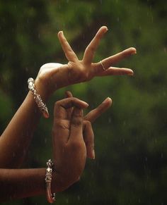 two hands making the v sign with their fingers on a rainy day in front of trees