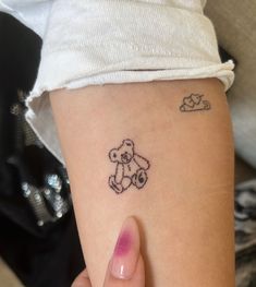 a person with a tattoo on their arm holding a small teddy bear in the air