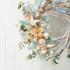 a wreath with flowers and seashells is hanging on a white wooden door frame