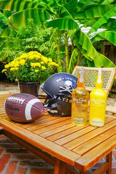 footballs, bottles and helmets sit on a picnic table in front of some plants