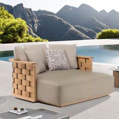 an outdoor lounge chair sitting next to a pool with mountains in the backgroud