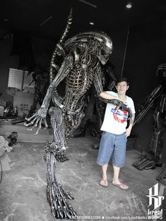 a man standing in front of a large metal alien statue with his hand on the arm