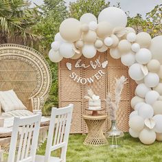 an outdoor party with white balloons and wicker walls, chairs and table set up in the grass