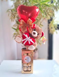 a teddy bear sitting on top of a box filled with chocolates next to a heart shaped balloon