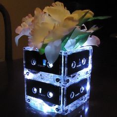 a vase filled with yellow flowers sitting on top of a table next to cassettes