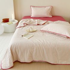 a bed with pink and white striped comforter next to a night stand on the floor