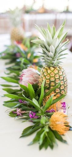 pineapples and other tropical flowers are lined up on a long white tablecloth